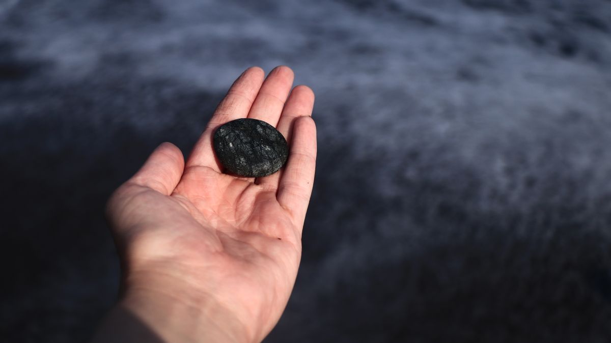 An open hand holding a smooth black stone, with the dark sea blurred behind it.